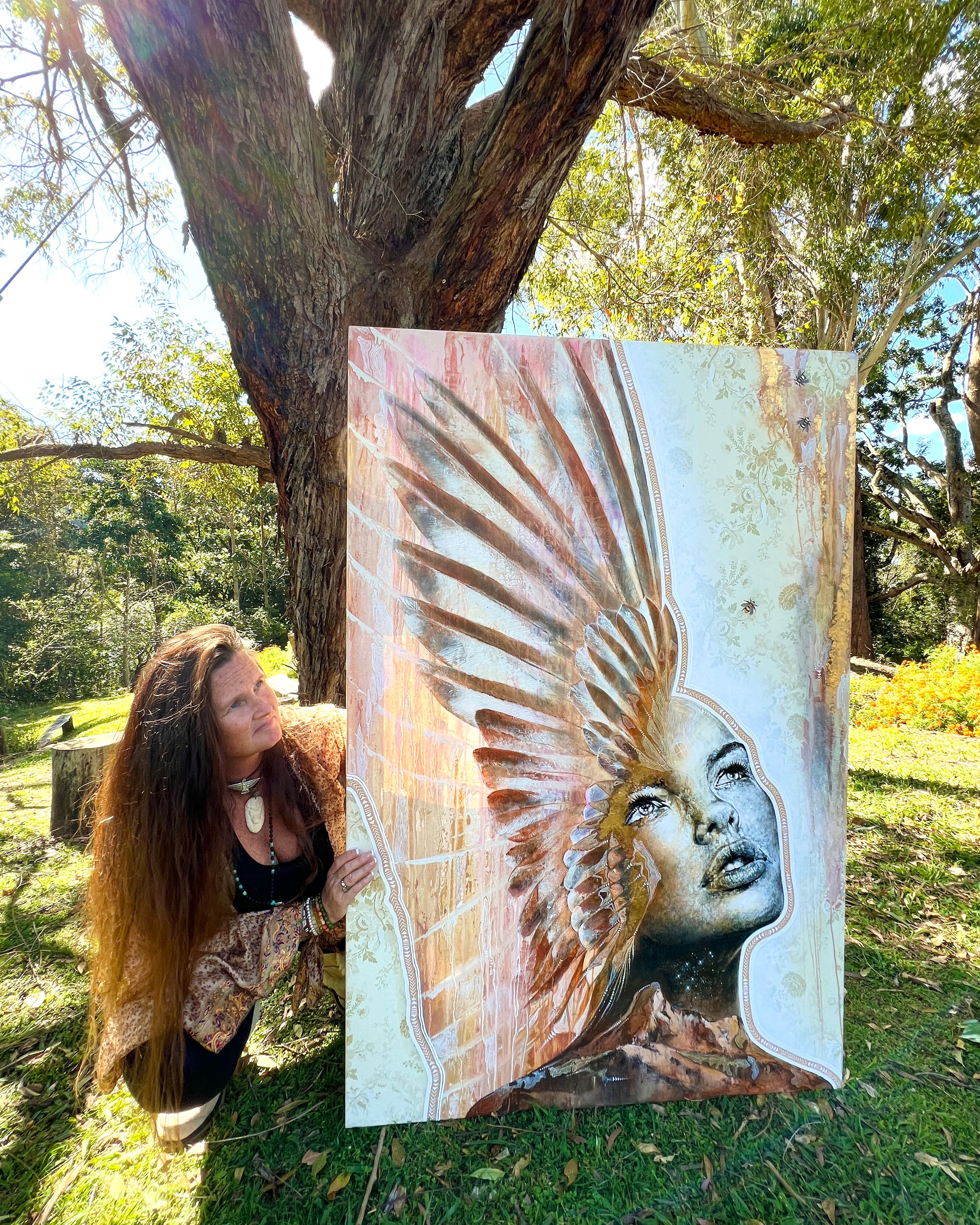 Person holding a large painting of a winged figure in a natural setting